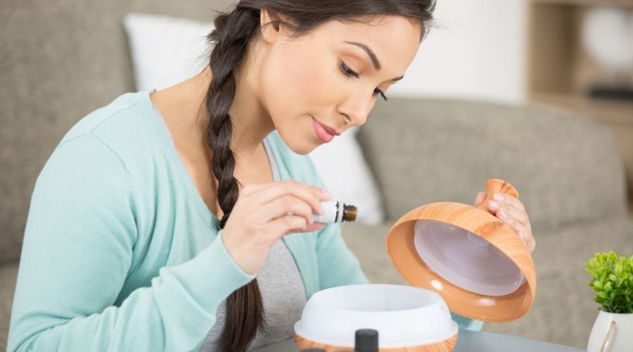 woman placing essential oils into diffuser - best essential oils for headaches and migraines